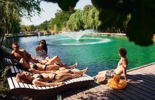 Sunny warm weather. Group of young happy people have fun in swimming pool at daytime photo