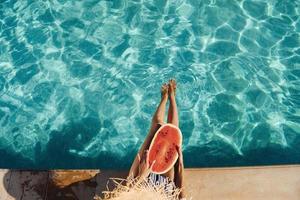 Young woman sits near swimming pool at daytime with watermelon photo