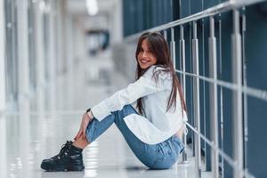 morena con camisa blanca se sienta adentro en un aeropuerto moderno o en un pasillo durante el día foto