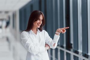 morena con camisa blanca posando en interiores en un aeropuerto moderno o en un pasillo durante el día foto