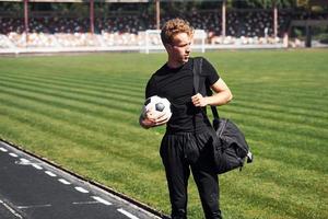 Football player on the field. Sportive young guy in black shirt and pants outdoors at daytime photo