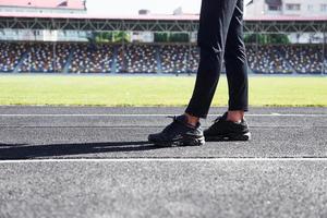 Close up view of legs of runner in black pants and shoes that is outdoors on the track photo