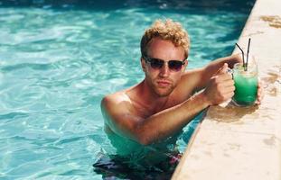 Guy in black sunglasses and with cocktail is in swimming pool photo