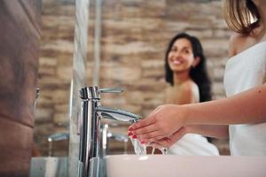 dos hermosas mujeres jóvenes juntas en el baño cerca del espejo y limpiándose la cara foto