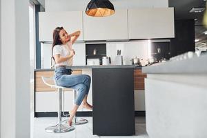 Young beautiful brunette in casual clothes sits in kitchen with fresh drink at morning time photo