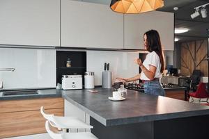 joven y hermosa morena con ropa informal preparando café en la cocina durante el día foto