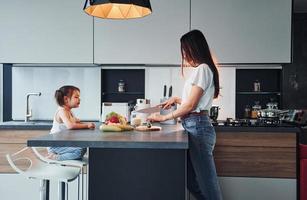 vista lateral de la madre que con su pequeña hija prepara comida en el interior de la cocina foto