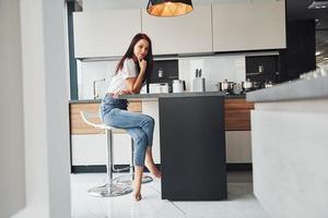 Young beautiful brunette in casual clothes sits in kitchen with fresh drink at morning time photo