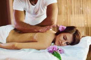 Purple flower lying down. Man does massage to the young woman in white towel indoors photo