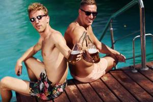 dos amigos varones se sientan cerca del agua al aire libre con bebidas en las manos foto