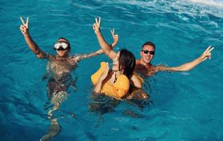 Using yellow colored duck to swim. Group of young happy people have fun in swimming pool at daytime photo