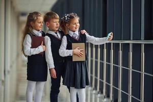 School kids in uniform together with phone and making selfie in corridor. Conception of education photo