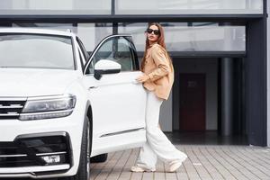 Outside near car. Fashionable beautiful young woman and her modern automobile photo