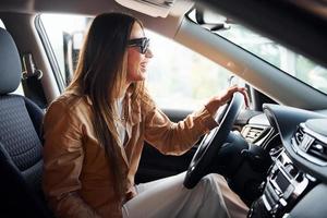 vista lateral de una hermosa joven de moda que está dentro de su automóvil moderno foto