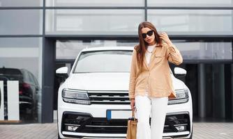 Outside near car. Fashionable beautiful young woman and her modern automobile photo