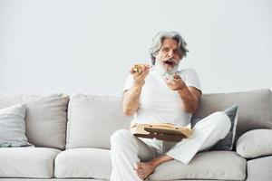 Soccer fan with pizza watches match. Senior stylish modern man with grey hair and beard indoors photo