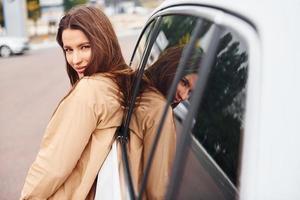 Leans on the door. Fashionable beautiful young woman and her modern automobile photo