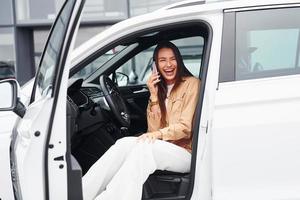 Talks by phone with door opened. Fashionable beautiful young woman and her modern automobile photo