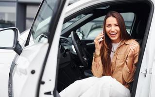 Talks by phone with door opened. Fashionable beautiful young woman and her modern automobile photo