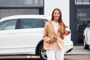 camina coche cercano. mujer joven hermosa de moda y su automóvil moderno foto