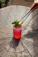 Waiter's hand. With lemon and mint. Close up view of fresh summer alcoholic cocktail on the wooden table photo