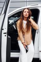 Outdoors against modern building. Fashionable beautiful young woman and her modern automobile photo