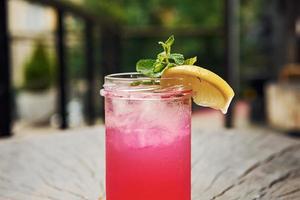 Pink colored liquid with lemon. Close up view of fresh summer alcoholic cocktail on the wooden table photo