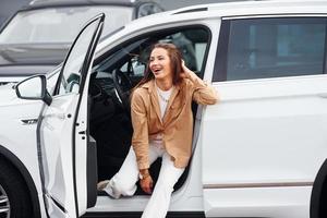 Outdoors against modern building. Fashionable beautiful young woman and her modern automobile photo