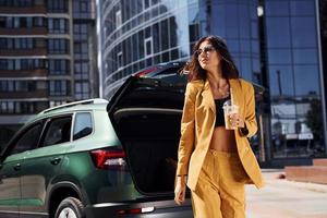 Conception of inspiration. Young fashionable woman in burgundy colored coat at daytime with her car photo
