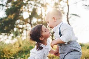 lindo hermano y hermana jugando juntos al aire libre con hermosos árboles y sol en el fondo foto