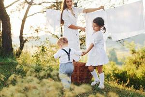 ama de casa secando ropa. la joven madre con su pequeña hija y su hijo está al aire libre en el bosque. hermoso amanecer foto