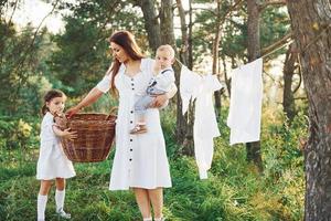 Housewife drying clothes. Young mother with her little daughter and son is outdoors in the forest. Beautiful sunshine photo