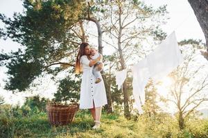 Clean clothes hanging on the rope to dry. Young mother with her little son is outdoors in the forest. Beautiful sunshine photo