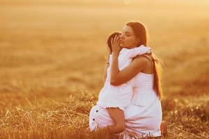 Positive little girl with her mother have weekend outdoors on the summer field together photo