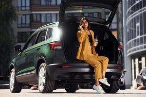 Talks by phone. Young fashionable woman in burgundy colored coat at daytime with her car photo