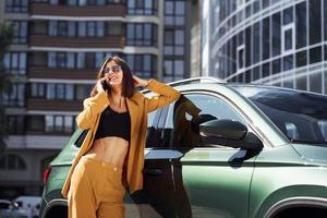 habla por teléfono. joven mujer de moda con abrigo de color burdeos durante el día con su coche foto