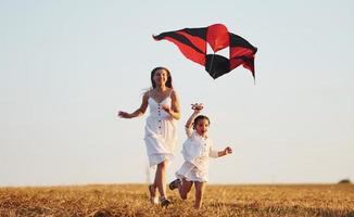 feliz madre con su pequeña hija diviértete jugando con cometas al aire libre en el campo foto