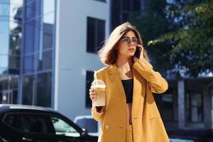 Coffee break. Young fashionable woman in burgundy colored coat at daytime with her car photo