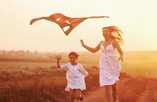 feliz madre con su pequeña hija diviértete jugando con cometas al aire libre en el campo foto