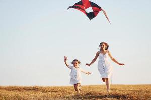 Happy mother with her little daughter have fun by playing with kite outdoors on the field photo