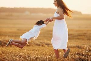 Positive little girl with her mother have weekend outdoors on the summer field together photo