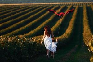 Calm daughter with her mother having a walk with kite on agricultural field at sunny daytime photo