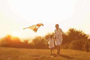 Daughter with her mother have fun together by running with kite on the field. Illuminated by beautiful sunlight photo