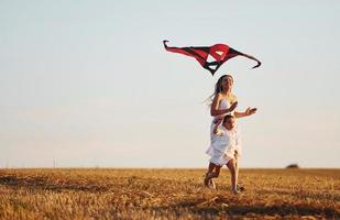 feliz madre con su pequeña hija diviértete jugando con cometas al aire libre en el campo foto