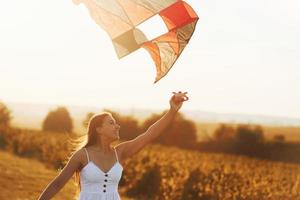 mujer alegre divirtiéndose con cometa al aire libre en el campo en verano y sonrisas foto