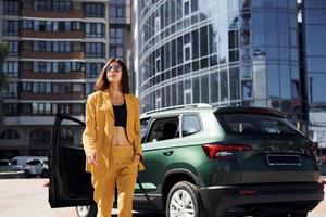 camina hacia adelante desde el automóvil. joven mujer de moda con abrigo de color burdeos durante el día con su coche foto