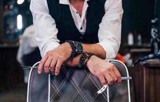 Close up view of man in luxury clothes that standing indoors in barbershop with scissors photo