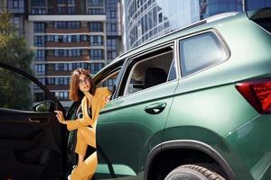 Walks out from automobile. Young fashionable woman in burgundy colored coat at daytime with her car photo