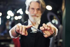 en barbería. un anciano moderno y elegante con pelo gris y barba está en el interior foto