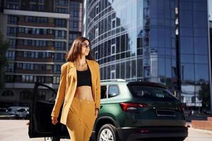 camina hacia adelante desde el automóvil. joven mujer de moda con abrigo de color burdeos durante el día con su coche foto